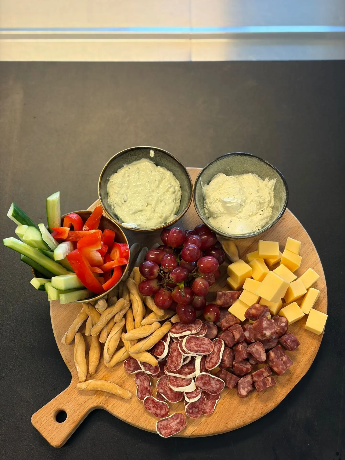 Borrelplank van bovenaf met kaas, worst, groente, druiven en dips